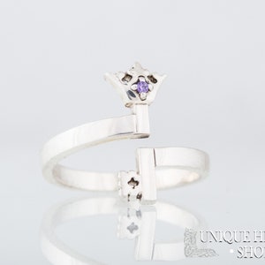 May include: A silver ring with a key design. The key has a small purple gemstone at the top, which is shaped like a crown.