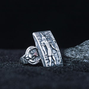 May include: Two silver rings with intricate designs. One ring features a detailed depiction of an Egyptian god, while the other ring has a red gemstone.