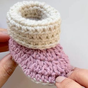 May include: A pair of crocheted baby booties with a pink and white color scheme. The booties are made with a soft yarn and have a simple design.