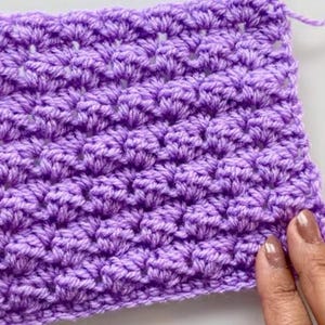 May include: A close-up of a purple crocheted fabric with a textured pattern. The fabric is made with a single crochet stitch and has a repeating pattern of small holes.
