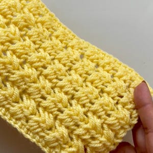 May include: A close-up of a yellow crocheted fabric with a textured pattern.