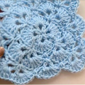 May include: A close-up of a light blue crocheted doily with a scalloped edge. The handmade piece features a detailed floral pattern with openwork, showcasing the intricate stitch work. The soft blue colour adds a delicate touch to the craft.