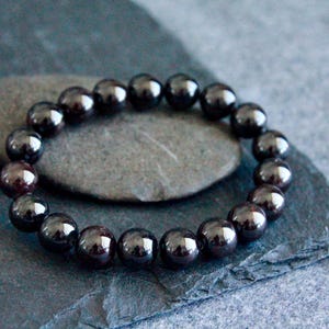 May include: A black gemstone bracelet with round beads. The bracelet is made of polished black stones and is resting on a dark gray surface.