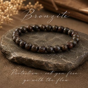 May include: A beaded bracelet made of round, dark brown, metallic-sheen bronzite stones. The image features the text Bronzite at the top and the text Protection - set you free - go with the flow at the bottom in a white cursive script font.