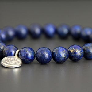 May include: A blue lapis lazuli gemstone bracelet with a silver charm featuring a lotus flower design.