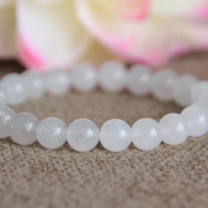 May include: White gemstone bracelet with round beads. The bracelet is made of white stones and is on a brown surface.