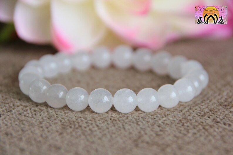 May include: White gemstone bracelet with round beads. The bracelet is made of white stones and is on a brown surface.