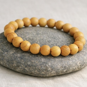 Op de afbeelding: Een armband met lichtbruine houten kralen, elk ongeveer 1,5 cm in diameter. De armband ligt op een grijze steen, tegen een neutrale achtergrond. De kralen tonen zichtbare houtnerf.