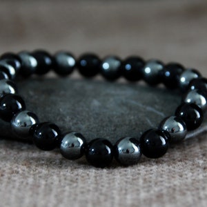 May include: A black and silver beaded bracelet with alternating black and silver beads. The bracelet is lying on a grey stone.