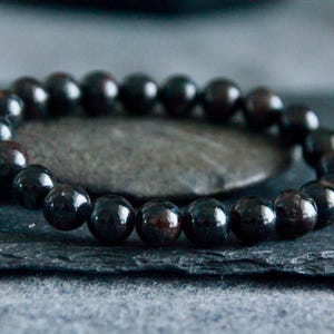 May include: A black beaded bracelet on a dark grey background.