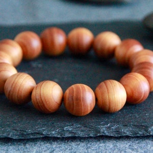 Puede incluir: Un brazalete de madera con 18 cuentas redondas. Las cuentas son de color marrón claro con vetas marrones más oscuras.