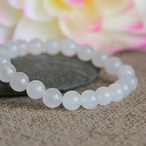 May include: White gemstone bracelet with round beads. The bracelet is made of white stones and is on a brown surface.