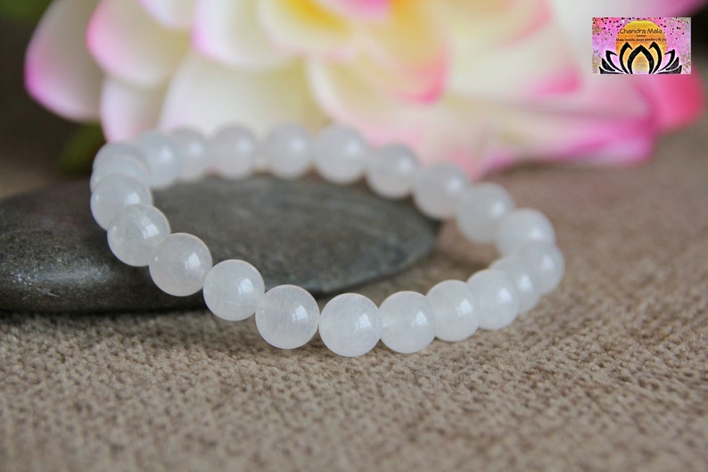 May include: White gemstone bracelet with round beads. The bracelet is made of white stones and is on a brown surface.