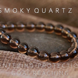 May include: Smoky Quartz bracelet with brown beads. The bracelet is on a brown fabric background. The text "SMOKY QUARTZ" is above the bracelet. The text "CENTERING - PROTECTION - GOAL REACHING" is below the bracelet.