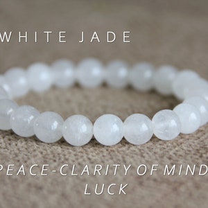 May include: White jade bracelet with the words "WHITE JADE" and "PEACE-CLARITY OF MIND-LUCK" printed below. The bracelet is made of white jade beads.