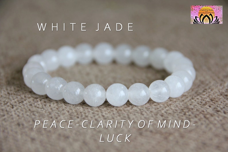 May include: White jade bracelet with the words "WHITE JADE" and "PEACE-CLARITY OF MIND-LUCK" printed below. The bracelet is made of white jade beads.