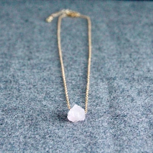 Könnte beinhalten: Eine zarte goldene Kettenkette mit einem kleinen, rohen Anhänger aus rosa Quarzkristall.