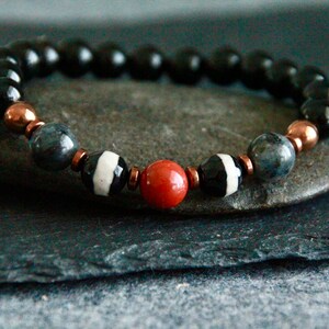 May include: A black onyx beaded bracelet with copper and white agate beads. The bracelet features a red carnelian bead in the center.