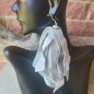 May include: A pair of long, gray leather tassel earrings with a silver hook and a small, round, white bead.