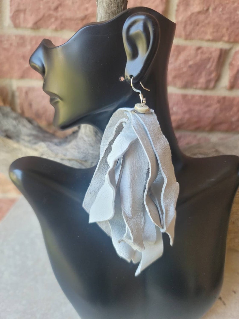 May include: A pair of long, gray leather tassel earrings with a silver hook and a small, round, white bead.