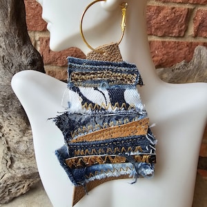 May include: A pair of large hoop earrings with a layered design featuring denim, leather, and gold accents. The earrings are handmade and have a bohemian style.