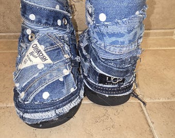 May include: A pair of denim boots with a patchwork design. The boots are made from blue denim with white polka dots and feature the "OshKosh B'gosh" label. The boots have a black sole and a distressed look.