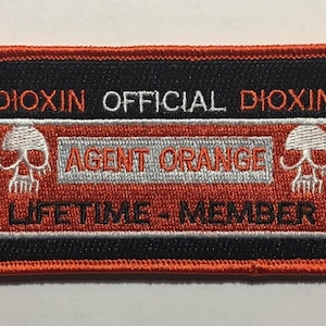 May include: A black and orange embroidered patch with the text "Dioxin Official Dioxin Agent Orange Lifetime Member" and two skull images.