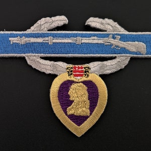 May include: A purple heart medal with a gold border and a silver wreath with crossed rifles above it. The medal is a military award for soldiers wounded or killed in action.