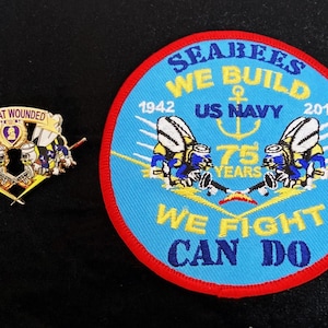 May include: A pin and a patch with military insignia. The pin reads "COMBAT WOUNDED" above a crest with figures. The patch is round, with a blue background and red border. It reads "SEABEES WE BUILD US NAVY 1942-2017 WE FIGHT CAN DO".