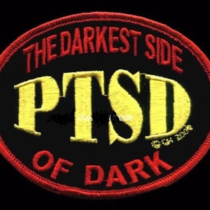 May include: A black and red oval patch with the text "The Darkest Side of PTSD" in yellow and red lettering.