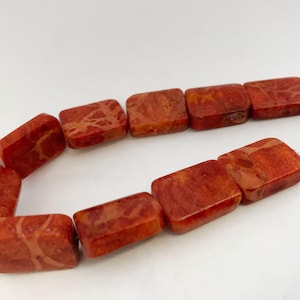 May include: A strand of rectangular beads in a vibrant orange-red hue. Each bead features a distinct, natural-looking marbled texture with lighter vein-like patterns running throughout the surface, arranged in a curved line.