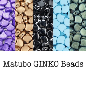 May include: A collection of Matubo GINKO beads in various colors: purple, gold, black, light blue, and gray-green. The beads have a unique, organic shape, perfect for jewelry making and crafting projects.