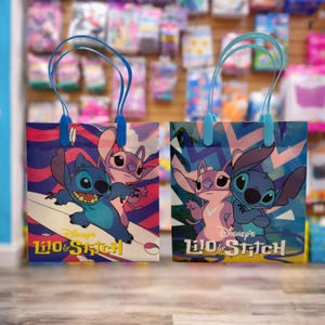 Op de afbeelding: Twee rechthoekige cadeautassen met de Disney-figuren Lilo & Stitch. De linker tas toont Stitch die surft met Angel, terwijl de rechter tas hen samen staand afbeeldt. Beide tassen hebben blauwe hengsels en het Lilo & Stitch logo op de voorzijde.