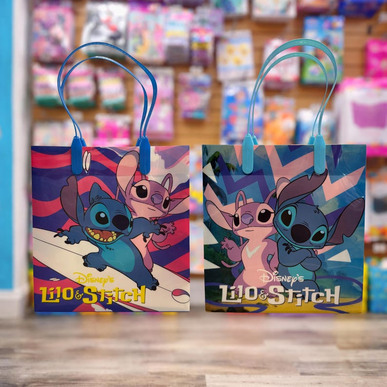 Op de afbeelding: Twee rechthoekige cadeautassen met de Disney-figuren Lilo & Stitch. De linker tas toont Stitch die surft met Angel, terwijl de rechter tas hen samen staand afbeeldt. Beide tassen hebben blauwe hengsels en het Lilo & Stitch logo op de voorzijde.