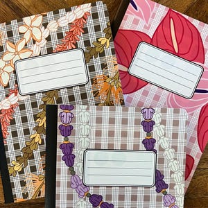 May include: Three notebooks with floral and geometric patterns. One notebook features a brown and white plaid design with orange and cream-colored flowers. Another has a pink floral pattern, and the third has a purple floral design. Each notebook has a blank label.