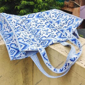 K&ouml;nnte beinhalten: Eine blau-wei&szlig; gemusterte Tragetasche mit passenden Tr&auml;gern. Die Tasche hat ein sich wiederholendes geometrisches Design in Blaut&ouml;nen auf wei&szlig;em Hintergrund. Die Tr&auml;ger sind hellblau mit einem &auml;hnlichen Muster.