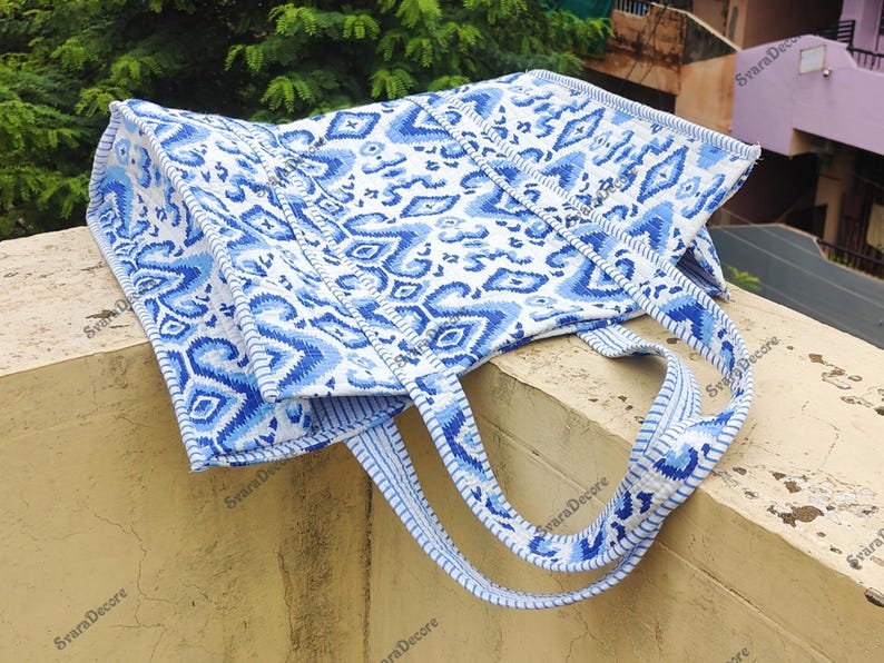 K&ouml;nnte beinhalten: Eine blau-wei&szlig; gemusterte Tragetasche mit passenden Tr&auml;gern. Die Tasche hat ein sich wiederholendes geometrisches Design in Blaut&ouml;nen auf wei&szlig;em Hintergrund. Die Tr&auml;ger sind hellblau mit einem &auml;hnlichen Muster.