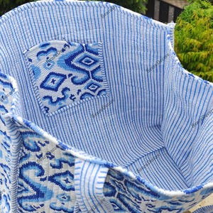K&ouml;nnte beinhalten: Offene Tragetasche mit blauem und wei&szlig;em Muster. Die Tasche hat eine Tasche mit geometrischem Muster und einen gestreiften Innenraum. Die Griffe und der Besatz sind ebenfalls gemustert. Die Tasche ist aus weichem, gestepptem Stoff gefertigt.