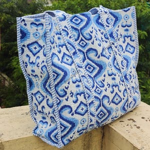 K&ouml;nnte beinhalten: Gro&szlig;e Tragetasche mit blau-wei&szlig;em geometrischen Muster. Die Tasche hat ein sich wiederholendes Design aus Rauten und Zickzackformen in verschiedenen Blaut&ouml;nen vor wei&szlig;em Hintergrund. Die Tasche hat stabile Griffe und einen verst&auml;rkten Boden.