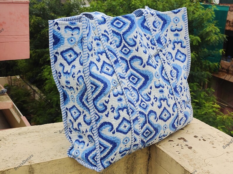 K&ouml;nnte beinhalten: Gro&szlig;e Tragetasche mit blau-wei&szlig;em geometrischen Muster. Die Tasche hat ein sich wiederholendes Design aus Rauten und Zickzackformen in verschiedenen Blaut&ouml;nen vor wei&szlig;em Hintergrund. Die Tasche hat stabile Griffe und einen verst&auml;rkten Boden.