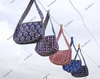 Könnte beinhalten: Vier handgefertigte Umhängetaschen mit gemustertem Stoff, die an einer Wäscheleine hängen. Die Taschen weisen verschiedene Designs in Blau, Rosa und Weiß auf, mit gestreiften Trägern und werden mit Wäscheklammern befestigt. Der Himmel ist im Hintergrund sichtbar.