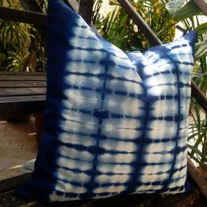 Op de afbeelding: Een vierkant decoratief kussen met een blauw-wit tie-dye patroon. Het kussen heeft een donkerblauwe rand en een rasterachtig ontwerp in blauw- en wittinten. Het kussen is gemaakt van zachte stof en is geschikt voor woondecoratie.