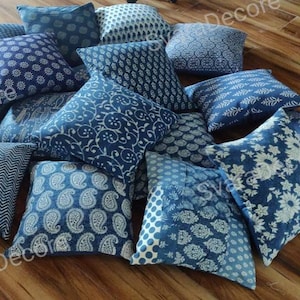 May include: A collection of blue and white patterned throw pillows with a variety of designs. The pillows are arranged on a wooden floor.