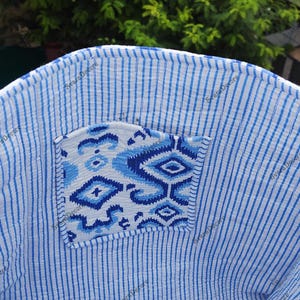 K&ouml;nnte beinhalten: Nahaufnahme eines blau-wei&szlig; gestreiften Stoffes mit einer gemusterten Tasche. Die Tasche weist ein geometrisches Design in Blaut&ouml;nen auf. Der Stoff scheint ein leichtes, m&ouml;glicherweise Baumwollmaterial zu sein. Die Gesamt&auml;sthetik ist l&auml;ssig und sommerlich.