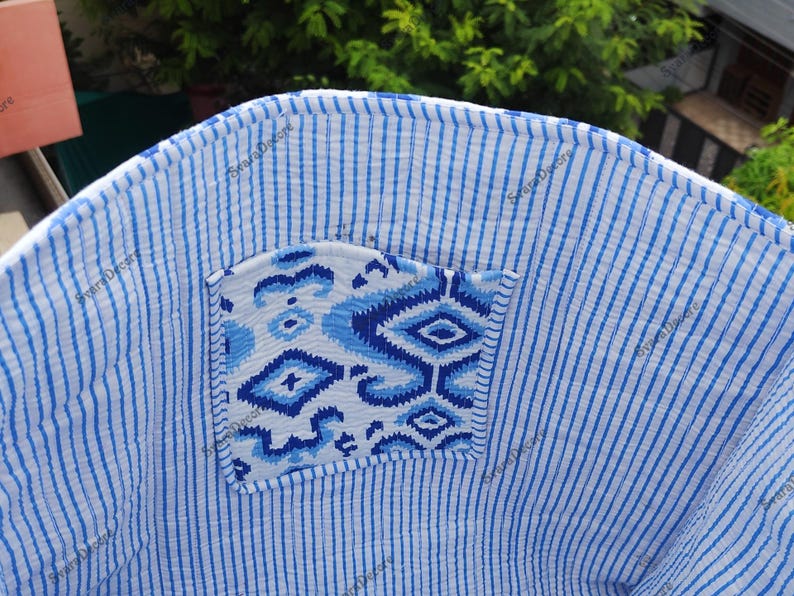 K&ouml;nnte beinhalten: Nahaufnahme eines blau-wei&szlig; gestreiften Stoffes mit einer gemusterten Tasche. Die Tasche weist ein geometrisches Design in Blaut&ouml;nen auf. Der Stoff scheint ein leichtes, m&ouml;glicherweise Baumwollmaterial zu sein. Die Gesamt&auml;sthetik ist l&auml;ssig und sommerlich.