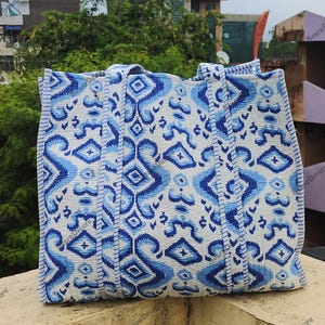 K&ouml;nnte beinhalten: Eine gro&szlig;e Tragetasche mit einem wei&szlig;en und blauen Muster. Die Tasche hat ein sich wiederholendes Muster aus stilisierten Formen in Blaut&ouml;nen auf wei&szlig;em Hintergrund. Die Tasche hat zwei Griffe und ist aus einem strukturierten Stoff gefertigt.