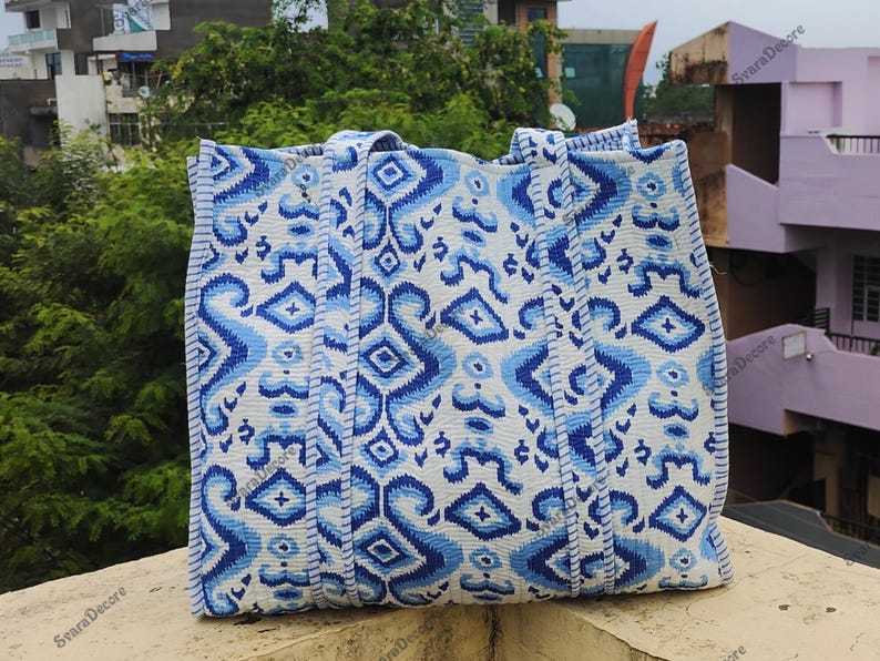 K&ouml;nnte beinhalten: Eine gro&szlig;e Tragetasche mit einem wei&szlig;en und blauen Muster. Die Tasche hat ein sich wiederholendes Muster aus stilisierten Formen in Blaut&ouml;nen auf wei&szlig;em Hintergrund. Die Tasche hat zwei Griffe und ist aus einem strukturierten Stoff gefertigt.