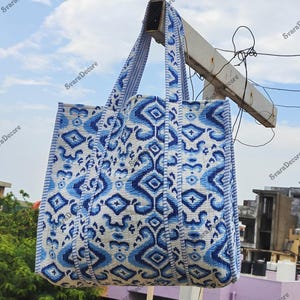 K&ouml;nnte beinhalten: Eine gro&szlig;e Tragetasche mit blau-wei&szlig;em geometrischen Muster. Die Tasche hat zwei Henkel und h&auml;ngt drau&szlig;en. Das Muster ist ein sich wiederholendes Design aus Rauten und anderen Formen. Die Tasche ist aus einem robusten Stoff gefertigt.
