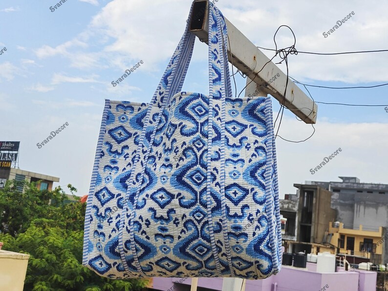 K&ouml;nnte beinhalten: Eine gro&szlig;e Tragetasche mit blau-wei&szlig;em geometrischen Muster. Die Tasche hat zwei Henkel und h&auml;ngt drau&szlig;en. Das Muster ist ein sich wiederholendes Design aus Rauten und anderen Formen. Die Tasche ist aus einem robusten Stoff gefertigt.