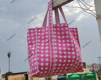 Könnte beinhalten: Eine große Tragetasche mit rosa und weißem Karomuster und passenden Griffen. Die Tasche besteht aus gestepptem Stoff und hängt im Freien vor einem bewölkten Himmel. Ein modisches Accessoire.